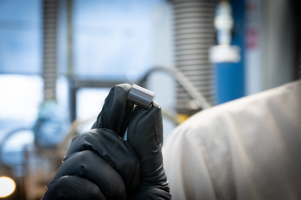 BWXT nuclear clean energy fuel pellet employee holding pellet black gloves white lab coat